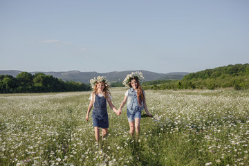 Naklejka na ściany i meble two cute teen girls in denim overalls walk in a daisy field