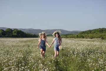 two cute teen girls in denim overalls walk in a daisy field