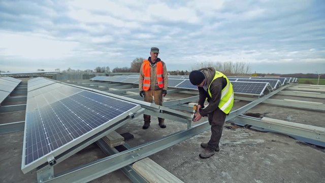 Worker attaches solar panel on metal base. Technicians install photovoltaic panel on the background of solar farm on a flat roof.