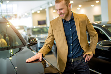 happy caucasian man owner of new car, stand next to new automobile, posing at camera. in dealership
