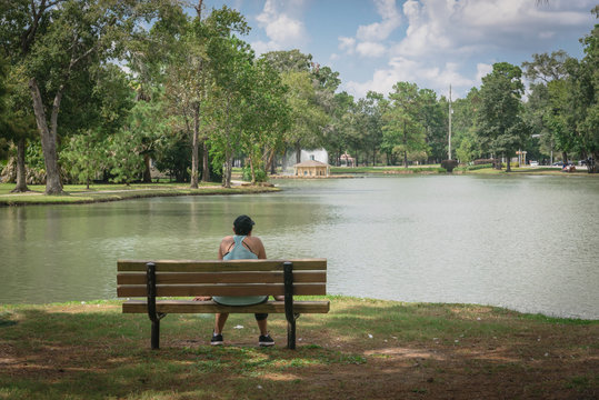 Behind a sporty lady with black cap on bench in lakeside urban park in Houston, Texas, USA