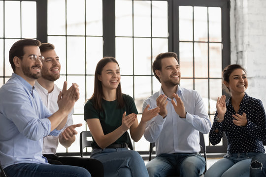 Overjoyed diverse young colleagues applaud celebrate victory or win at meeting, smiling multiracial businesspeople clap hands greeting congratulate business speaker or trainer, acknowledgment concept