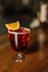 Americano cocktail decorated with slice of fresh orange on the bar table. Beautiful foam and bubbles. Dark wooden background.