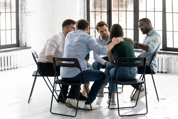 Diverse young people sit in circle participate in psychological therapy session together, multiethnic patients support comfort upset female client, engaged in group psychotherapy counseling