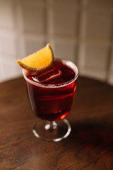 Americano cocktail decorated with slice of fresh orange on the bar table. Beautiful foam and bubbles. Large cube of ice. White tiles background.