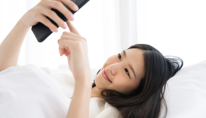 Fototapeta premium Young Asian woman using smart phone in bedroom at home happy and smile.