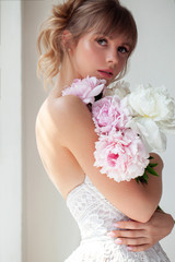 Beautiful girl holding peonies, attractive woman with big bouquet, female smells flowers, studio with sunlight.
