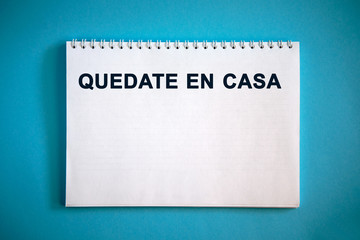 QUEDATE EN CASA text on a notepad on a blue background