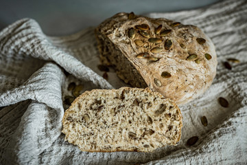 A slice of a fresh loaf of home-made whole grain bread with walnuts and sunflower seeds, on a beige towel, horizontal rustic style photo