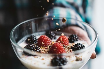 Close up shot of granola falling into a glass bowl of fruit and yogurt