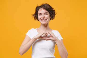 Smiling young brunette woman girl in white t-shirt posing isolated on yellow orange background in...