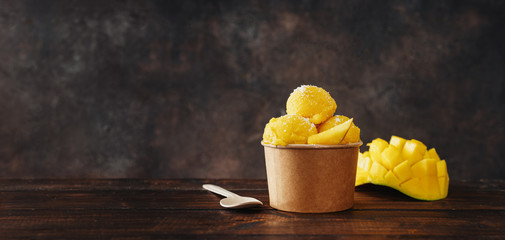Delicious vegan mango sorbet in a craft paper cup on dark background - obrazy, fototapety, plakaty