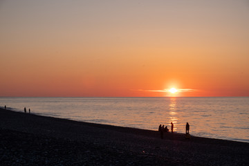 Sunset on the black sea. People walk along the beach and pier. Quiet, calm evening.