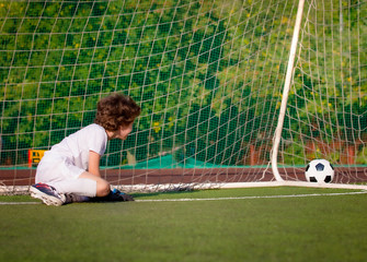 junior soccer goalkeeper. Disappointed boy in white goalie sportswear. Goalkeeper missed a goal during friendly match.