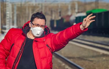 a man in a medical anti virus mask waves, stops a train on the tracks of a railway station