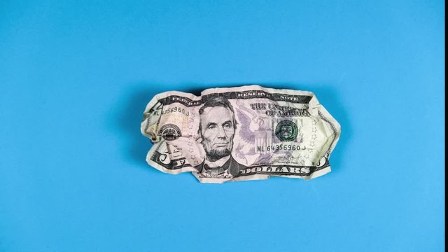Animation stop-motion technique crumpling paper five American dollars on blue background. Concept of fall of American currency, collapse of exchange and American stocks, financial crisis in country