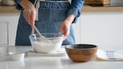 Hands of a young woman mix the ingredients in a bowl for future dough in a homemade vintage kitchen in the village. Bread. 4K.
