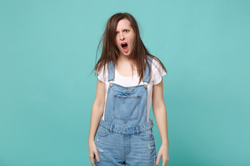 Shocked displeased young brunette woman girl in casual denim clothes posing isolated on blue turquoise background studio portrait. People lifestyle concept. Mock up copy space. Keeping mouth open.