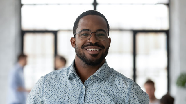 Headshot portrait of smiling African American businessman in glasses posing looking at camera in office, happy biracial male boss or CEO feel motivated show confidence and success, leadership concept