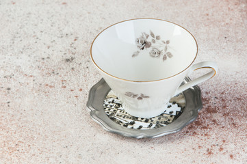 Antique tea mug on pewter coaster on concrete background.