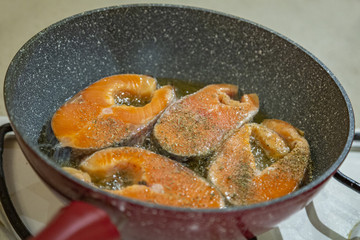 A steak of delicious fish varieties is fried in a frying pan on a kitchen gas stove