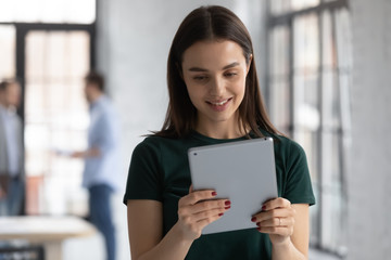 Smiling concentrated Caucasian female employee surfing wireless Internet on modern tablet gadget at workplace, happy woman worker texting or messaging, browse web using pad device in office
