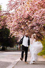 cheerful newlyweds running around the city happy among the flowering trees. Newlyweds have fun spending their time in a beautiful city. wedding in spring. emotional couple. selective focus