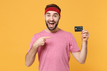 Excited young bearded fitness sporty guy sportsman in headband t-shirt in home gym isolated on...