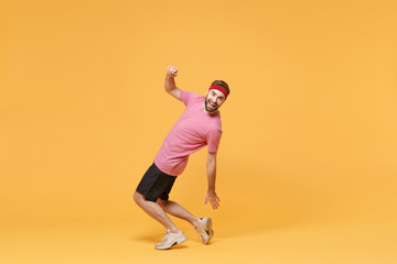 Fototapeta na wymiar Side view of funny fitness sporty guy sportsman in headband t-shirt in home gym isolated on yellow background. Workout sport motivation concept. Doing warm up cardio exercising reaching hand for heel.