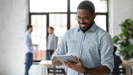 Smiling African American male employee use modern tablet gadget with wireless Internet connection...