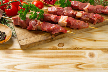 Raw kebab from meat on a wooden background with vegetables.