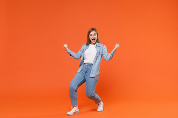 Fototapeta na wymiar Joyful young woman girl in casual denim clothes posing isolated on bright orange wall background studio portrait. People sincere emotions lifestyle concept. Mock up copy space. Doing winner gesture.