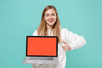 Cheerful young woman girl in casual white hoodie isolated on blue turquoise background. People lifestyle concept. Mock up copy space. Hold laptop pc computer with blank empty screen, showing thumb up.