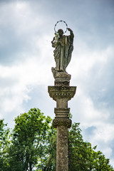 high antique statue with a baby in her arms on a background of blue sky and green trees
