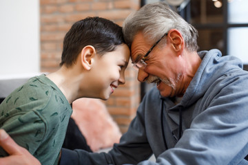 Happy grandfather sit on sofa and enjoy spending time with preschooler grandson at home, looking eyes to eyes