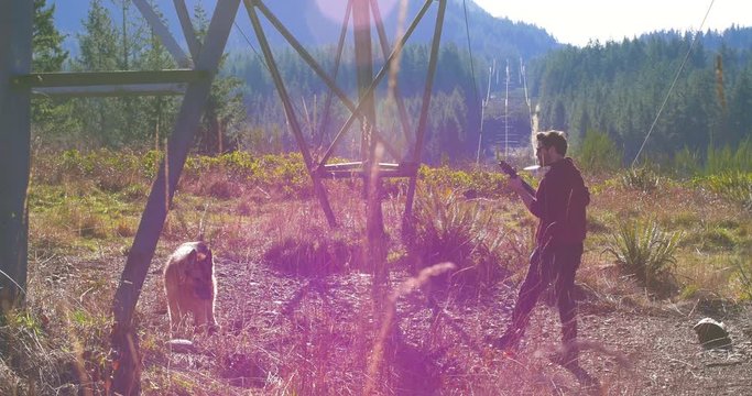 Man Plays Guitar to his Dog in the Seattle Sunshine. Mountains and sun rays are casted in the background. A happy man connects musically with his German Shepherd.