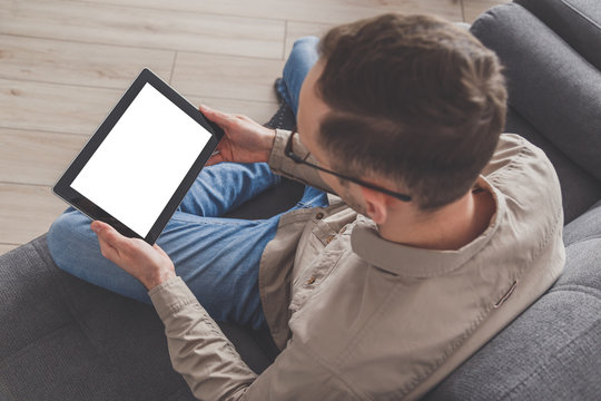 Internet surfing and conference calling. A man uses a tablet computer while sitting on a sofa at home. Dressed in everyday clothes. Tablet with blank screen