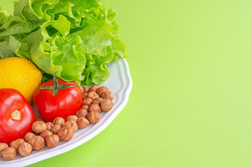 Keto diet. Juicy tomatoes, lemon, lettuce and nuts are on a white platter, on a green background.Horizontal, copy space