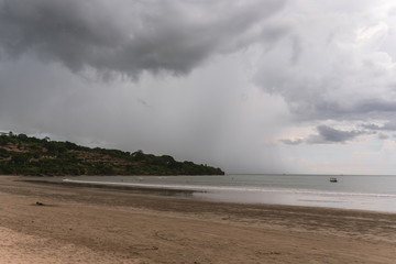 Deserted beach on the island of Bali. Clouds and clouds with rain of dark blue color. Sandy beach with sea and ocean. Tropical view. Hurricane.