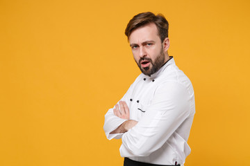 Side view of displeased confused bearded male chef cook or baker man in white uniform shirt isolated on yellow background. Cooking food concept. Mock up copy space. Hold hands crossed, looking camera.