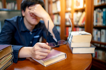 Smart Asian man university student feeling stressed and anxious while reading book by vintage...