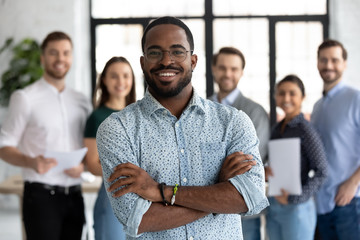 Smiling motivated African American male employee stand forefront posing together with colleagues in...