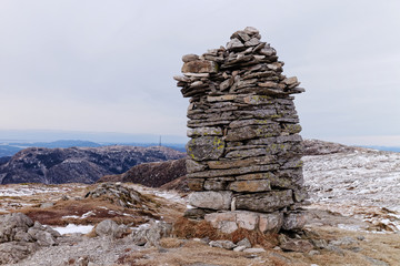 summit marker, stone marker, rock cairn in the right on path to Vidden trail tour between Mount Ulriken and Mount Fløyen, Bergen, Norway, Scandinavia, with mountain view on background