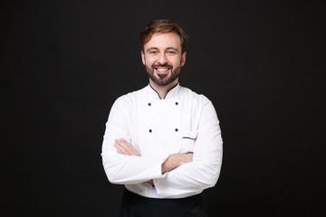 Smiling young bearded male chef cook or baker man in white uniform shirt posing isolated on black...