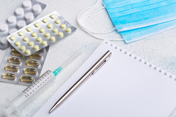 Medical face shield, disposable syringe, pills, pen and notebook on white background. The concept...