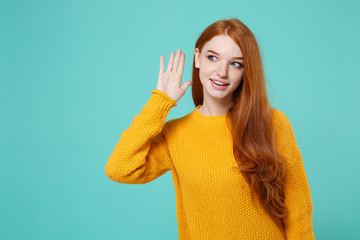 Curious young redhead woman girl in yellow sweater posing isolated on blue turquoise wall...