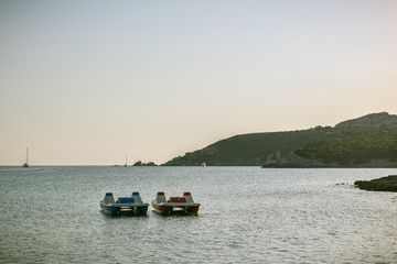 Fototapeta na wymiar Two pedal boats floating on the water in evening close to shore near Capo Testa in Sardinia