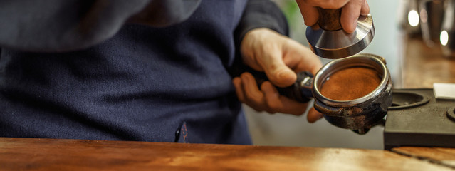 Coffee barista is pressing coffee bean into the filter block by using a temper. Close up and...