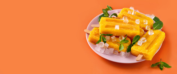 Vegan mango sorbet popsicles on trendy vivid orange background