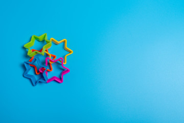 Four multi-colored plastic cookie cutter for making cookies in the shape of stars on a blue background. Culinary concept. Flat lay with copyspace.